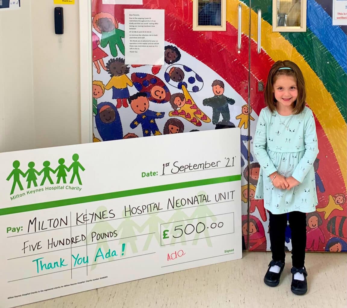 A little girl standing next to a donation cheque in a hospital setting