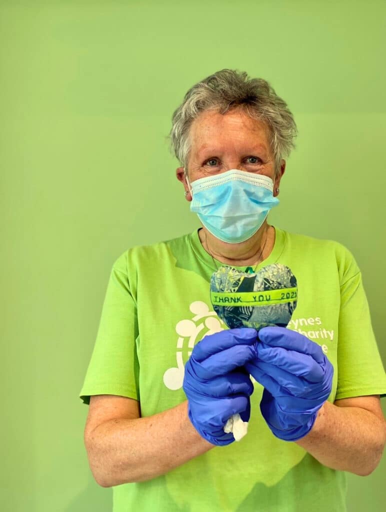 A lady wearing a face mask and gloves holding a heart which says thank you