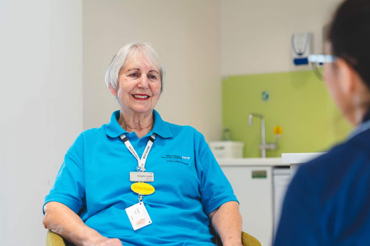 A lady in a blue volunteering top in a hospital environment