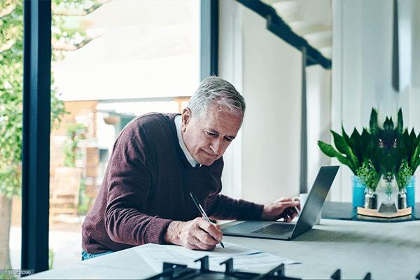 A man at a laptop writing on a piece of paper